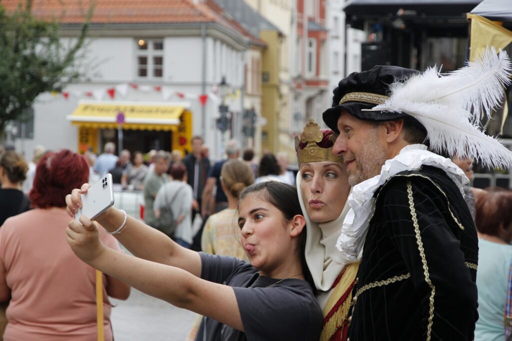 Utkädd kung och drottning tar selifes med en ung flicka på en marknad